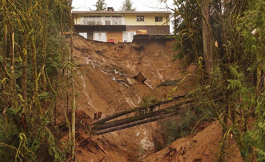 A steep, muddy cliff at the end of a residential yard where the embankment gave way